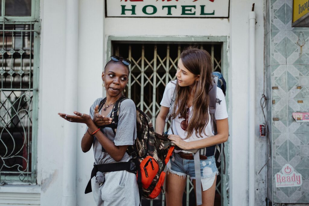 pexels photo 4881147 4881147 Two women stand laughing with backpacks, exploring a city during their travel adventure.
